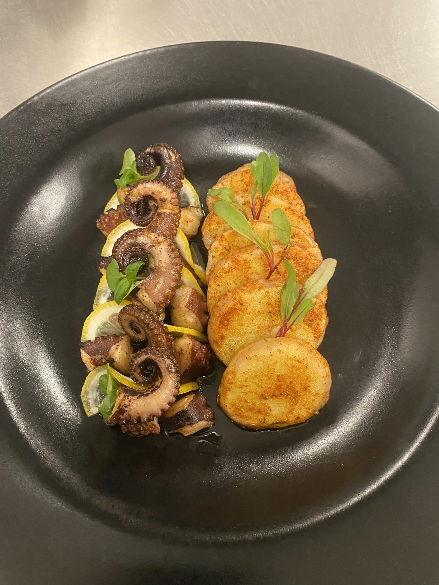 Pulpo al comal con papas y pimentón sobre plato negro